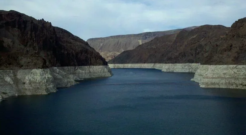 Calm lake between dark canyon walls with a pale mineral band along the shoreline