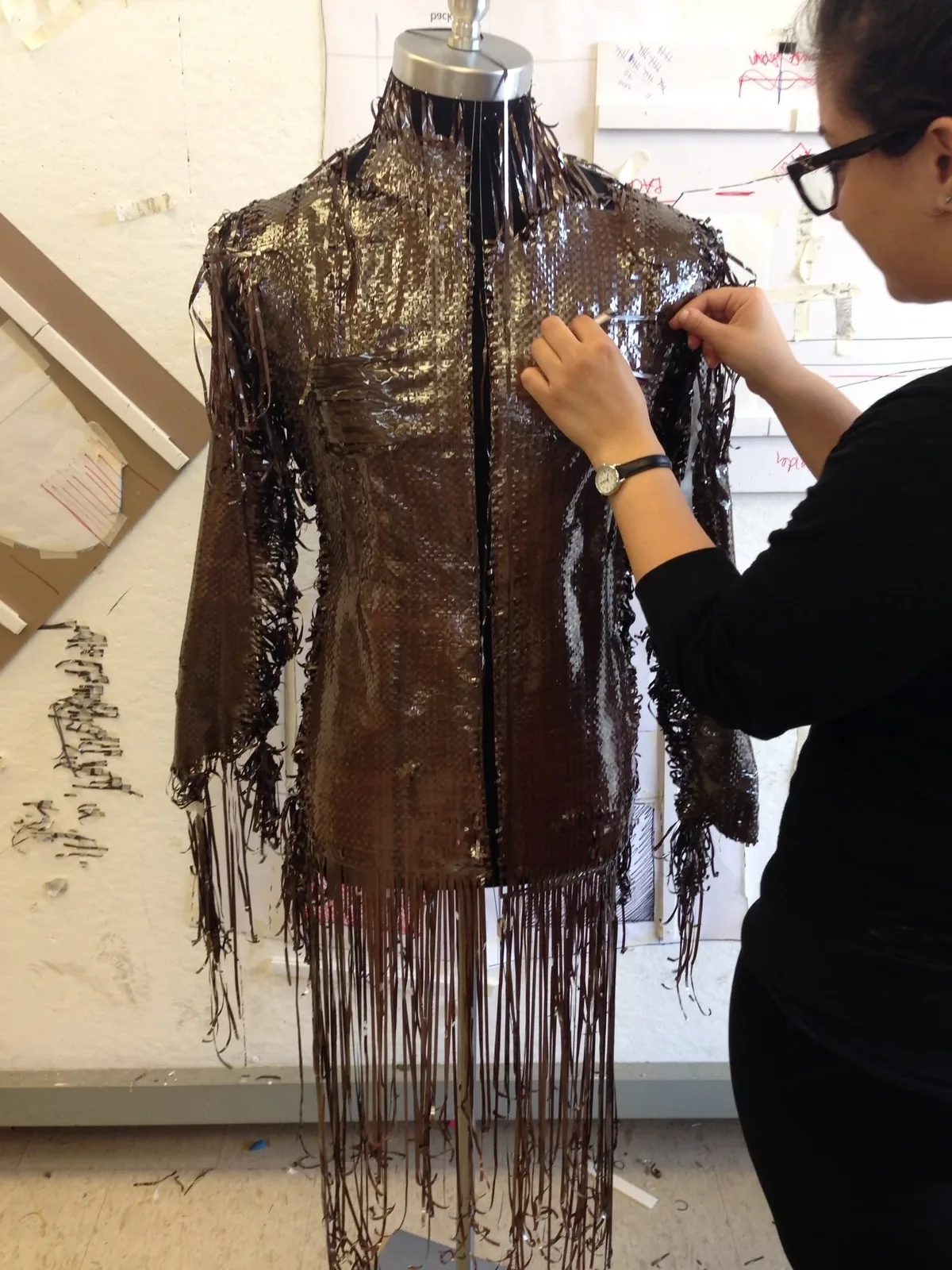 Person weaving dark tape onto a dress form to make a fringed jacket